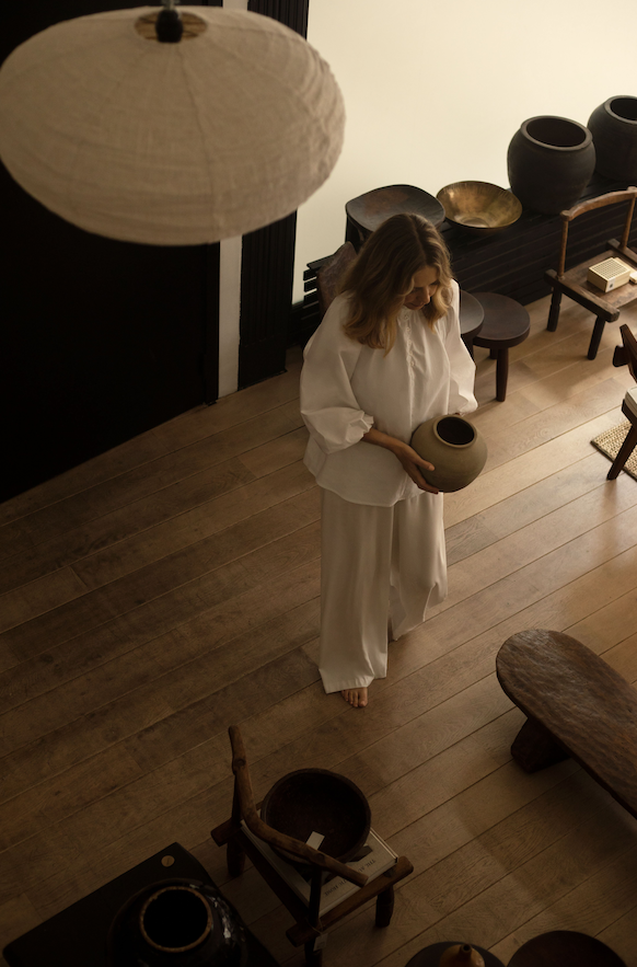 Andrea Lennon holding a handmade ceramic pot in her serene Brussels interior — reflecting craftsmanship, calm and soulful design
