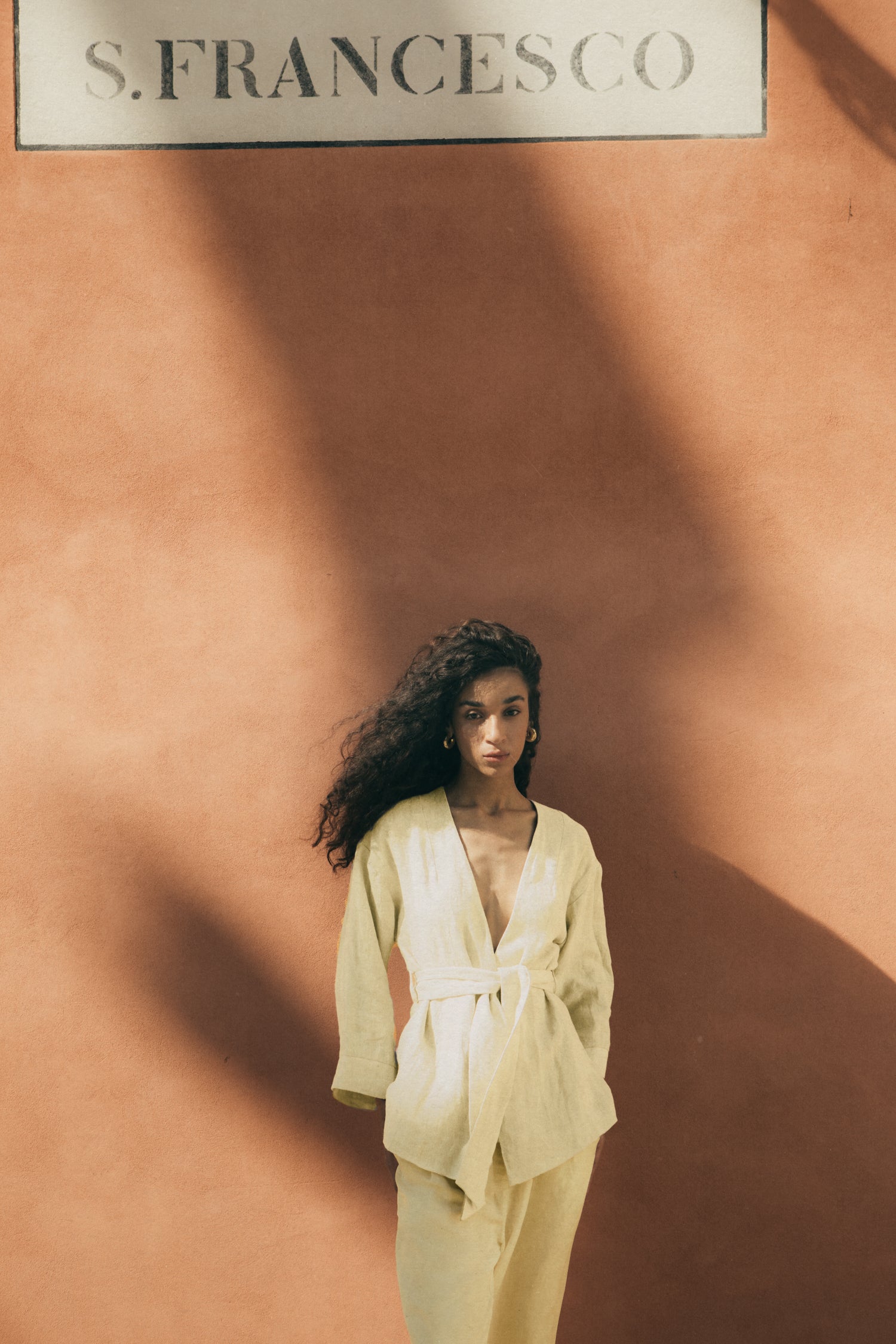 Rhúne SS24 collection — yellow wrap top photographed against a warm terracotta backdrop