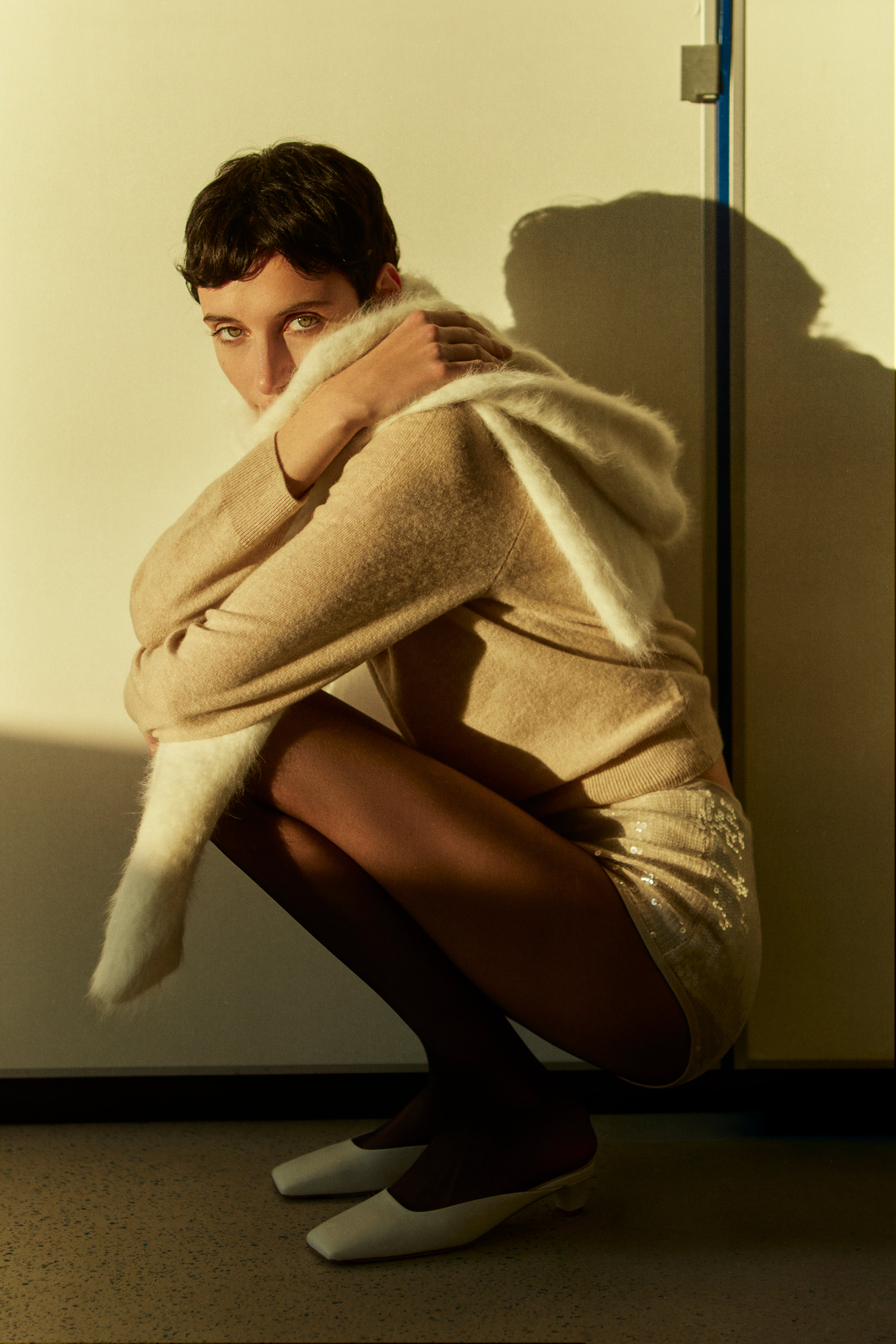 Rhúne AW25 Cashmere Capsule — timeless beige cashmere knit styled with sequined shorts in warm evening light